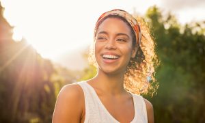 Portrait of beautiful african american woman smiling and looking away at park during sunset. Outdoor portrait of a smiling black girl. Happy cheerful girl laughing at park with colored hair band.